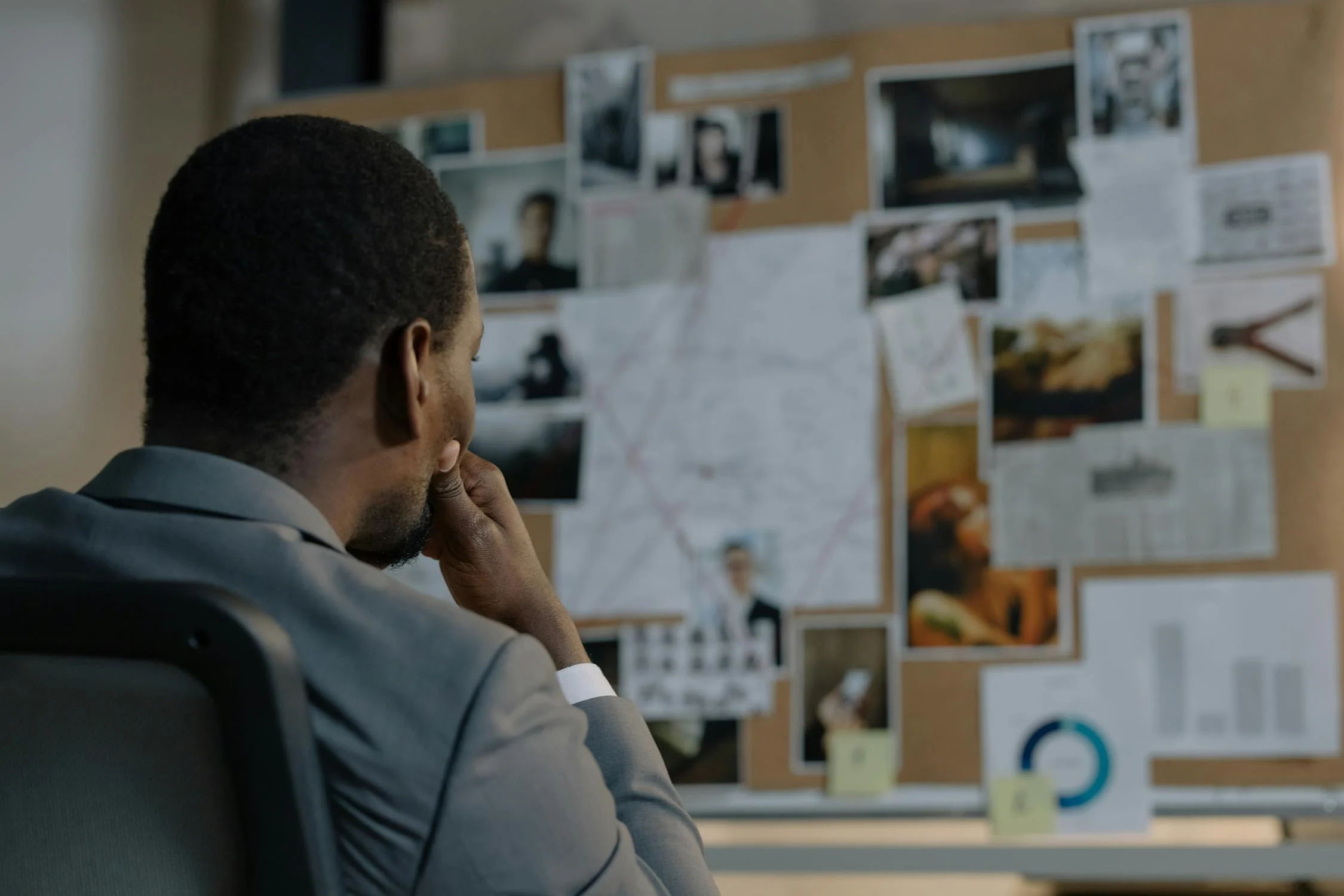 A detective examines a case board covered with photographs, notes, and evidence during a criminal investigation